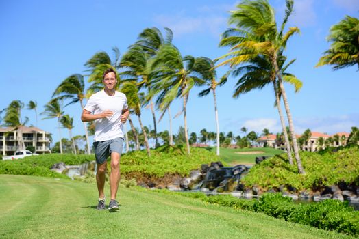 Outdoor exercise man running on grass in city park, resort area or upscale community. Happy young male runner staying fit exercising and living a healthy lifestyle training outside in summer nature.