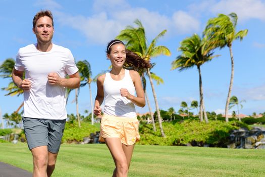 People running in city park. Happy young couple living an active healthy lifestyle jogging training their cardio during summer on road or neighborhood street. Multiracial group, Asian and Caucasian.