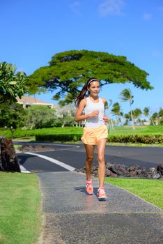 Jogger woman running on sidewalk in city street. Asian mixed race female adult runner in upscale residential neighborhood jogging along the street keeping a healthy lifestyle by exercising cardio.