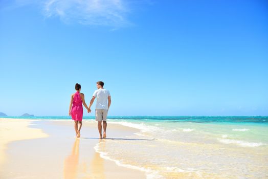 Honeymoon couple holding hands walking on perfect white sand beach. Newlyweds happy in love relaxing on summer holidays in sunny tropical paradise destination. Travel vacation concept.