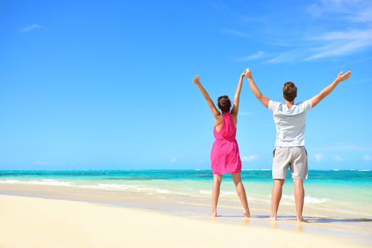 Happy free couple cheering on perfect beach travel holiday. Rear view of unrecognizable young people with arms raised to the sky praising the sun or showing success and freedom during summer vacation.