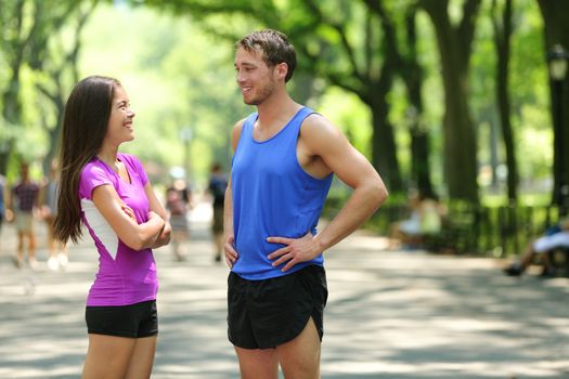 Happy runners couple talking after run in NYC park. Female and male adult athletes resting together in Central Park, New York city, wearing active tops and shorts sportswear for a summer workout.