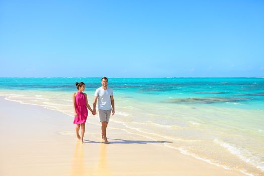 Summer vacation couple walking on beach landscape. Young adults relaxing together enjoying their holidays in perfect getaway in sunny tropical destination with pristine turquoise ocean water.
