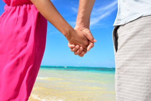 Holding hands romantic newlyweds couple on beach. Closeup of male and female hands with a sunny blue beach background as honeymoon concept or happy relationship during travel summer holidays.