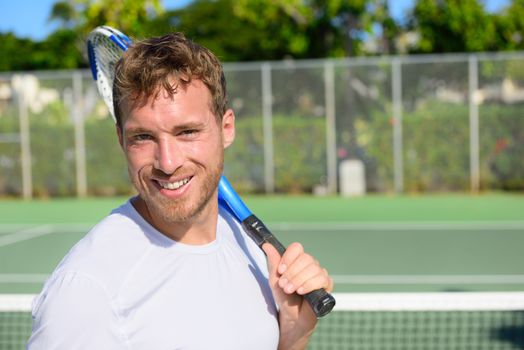 Portrait of male tennis player holding tennis racket after playing at game outside on hard court in summer. Fit man sport fitness athlete smiling happy living healthy active lifestyle outside.