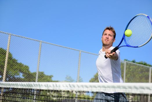 Tennis player man hitting ball in a volley. Male sport fitness athlete playing tennis on outdoors hard court in summer. Healthy active lifestyle concept.