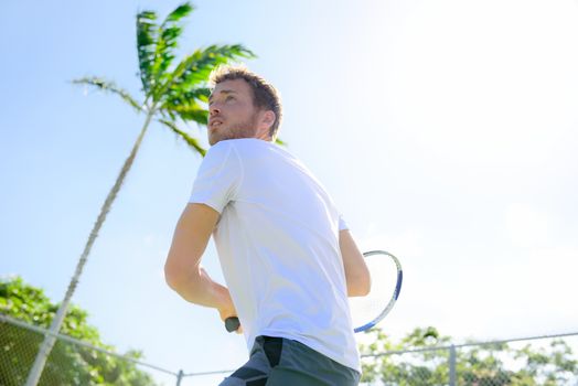 Male tennis player finishing serve playing outdoor. Man serve for game during outside tennis game. Fit male athlete living healthy fitness sport lifestyle. Young Caucasian model in his 20s.