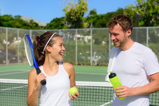 Tennis sport - couple relaxing after playing game of tennis outside in summer. Happy smiling friends on outdoor tennis court living healthy active fitness lifestyle. Woman and man athletes.