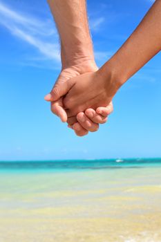 Love - romantic couple holding hands on beach. Close up of hands of young lovers enjoying romance on summer vacation travel holidays.