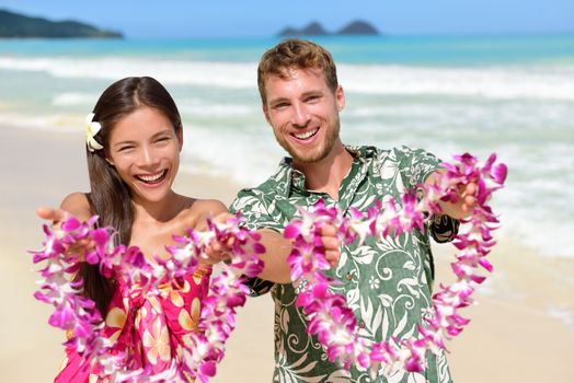 Welcome to Hawaii - Hawaiian people showing leis flower necklaces as a welcoming gesture for tourism. Travel holidays concept. Asian woman and Caucasian man on white sand beach in Aloha clothing.