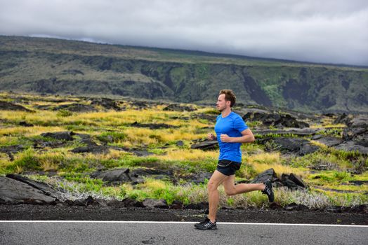 Athlete male runner running on mountain road. Running man jogging fast training cardio for marathon on countryside path in nature landscape, volcano background. Young Caucasian adult in his 20s.