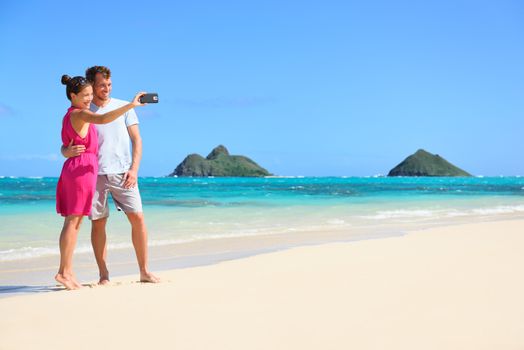 Couple on beach vacation taking selfie photograph using smartphone, Lanikai beach, Oahu, Hawaii, USA with Mokulua Islands. Couple holding smart phone camera.