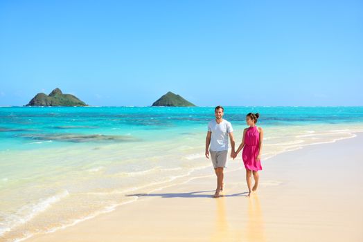 Summer vacation couple walking on beach landscape. Young adults relaxing together enjoying their holidays by pristine turquoise water on Lanikai beach, Oahu, Hawaii, USA with Mokulua Islands.