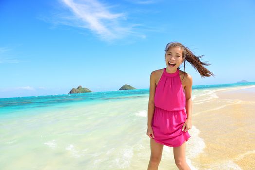 Woman having fun portrait on Hawaii Lanikai beach. Young mixed race female by water wearing pink sundress laughing during summer travel holidays on Oahu, Hawaii, USA with Mokulua Islands.