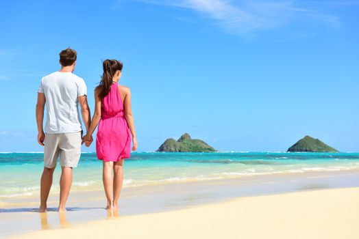 Beach summer holiday - couple on Hawaii beach vacation standing in white sand relaxing looking at ocean. Romantic young adults holding hands on Lanikai beach, Oahu, Hawaii, USA with Mokulua Islands.