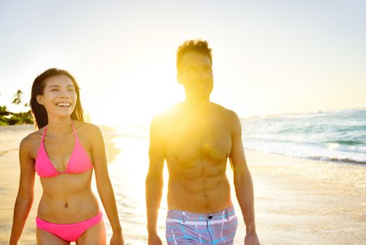 Beach Lifestyle Couple Walking on Beach at Sunset enjoying healthy active lifestyle in summer sun. People in beachwear, woman in bikini and man in casual swim shorts.