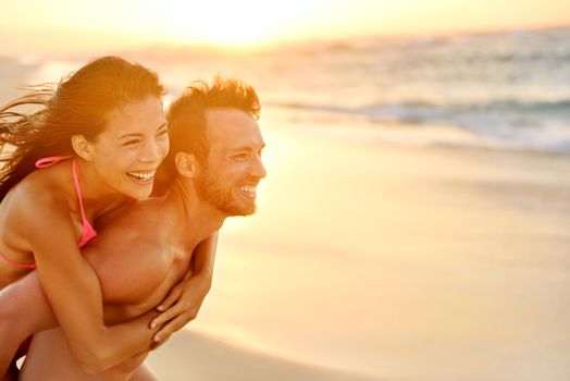 Lovers couple in love having fun piggybacking on date on beach. Portrait beautiful healthy young adults girlfriend and boyfriend hugging happy. Multiracial dating or healthy relationship. From Hawaii.