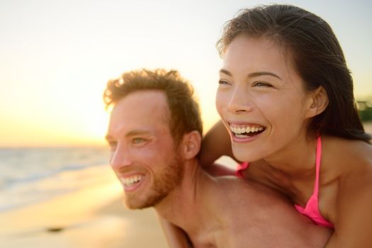 Beach couple laughing in love having fun romance on travel honeymoon vacation summer holidays. Young happy people, Asian woman and Caucasian man embracing outdoors on tropical beach in casual wear.