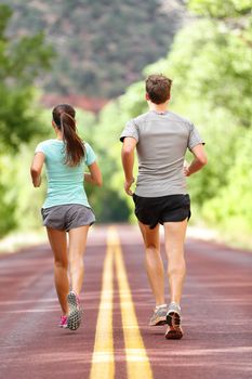 Runners running and jogging for health and fitness. People on fitness run on road in nature. Couple, woman and man training outside for fitness and healthy life. Full body length rear view of back.