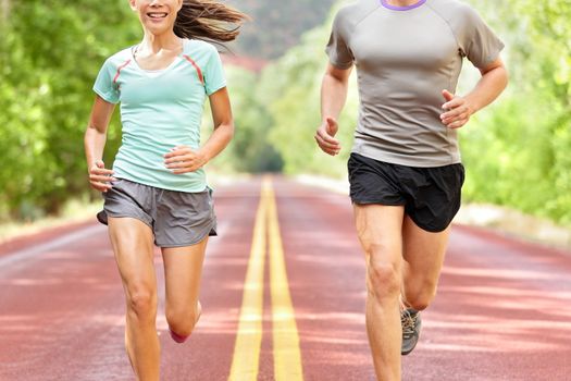 Health and fitness running. Runners on run training during fitness workout outside on road. People jogging together living healthy active lifestyle outside in summer. Midsection of woman and man.