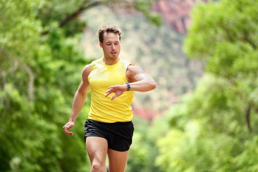 Running looking at heart rate monitor smartwatch while running. Male runner jogging outside looking at sports smart watch during workout training for marathon run. Fit male fitness model in his 20s.