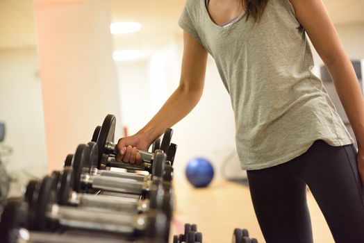 Gym woman strength training lifting dumbbell weights getting ready for exercise workout. Female fitness girl exercising indoor in fitness center. Beautiful fit mixed race Asian Caucasian model.