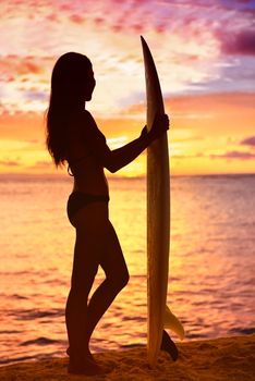 Surfer girl surfing looking at ocean beach sunset. Silhouette of female bikini woman looking at water with standing with surfboard having fun living healthy active lifestyle. Water sports with model.