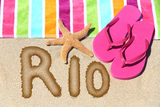 Rio beach concept. Overhead view ot the word RIO written on golden sand with a starfish, pink flip flops and towel conceptual of a summer vacation and travel in Rio de Janiero, Brazil
