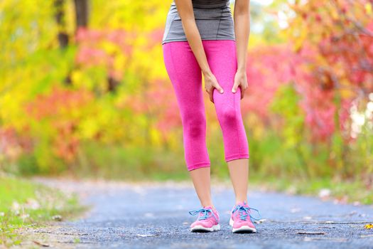 Muscle injury of female sports runner thigh. Woman running muscle strain injury in thigh. Closeup of runner touching leg in muscle pain outside in fall forest.