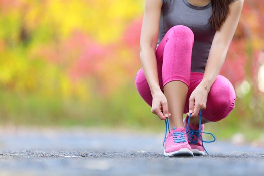 Running shoes - woman tying shoe laces. Closeup of female sport fitness runner getting ready for jogging outdoors on forest path in late summer or fall.