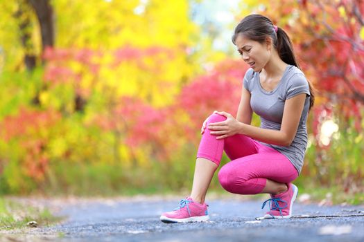 Sports running knee injury on woman in pain. Female runner with pain from sprain knee. Close up of legs, muscle and knee outdoors in late summer autumn forest.