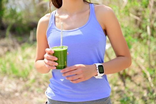 Green smoothie - woman runner wearing smartwatch. Healthy woman drinking vegetable smoothie wearing smart watch heart rate monitor during outdoor running workout in forest.