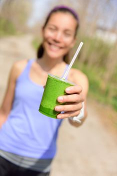 Green vegetable smoothie - healthy eating concept. Close up of green vegetable detox smoothie with spinach. Woman hand holding vegetable smoothies outdoors in forest.