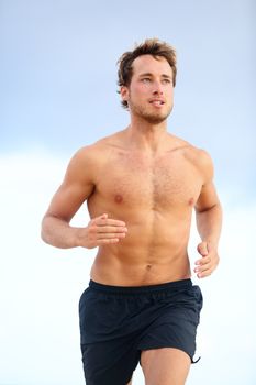 Fitness sports runner man jogging on beach. Handsome young fit sporty male athlete running outside on beautiful beach training. Caucasian male model in his 20s.