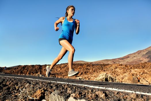 Running sprinting woman - female runner training outdoors jogging on mountain road in amazing landscape nature. Fit beautiful fitness model working out for marathon outside in summer.