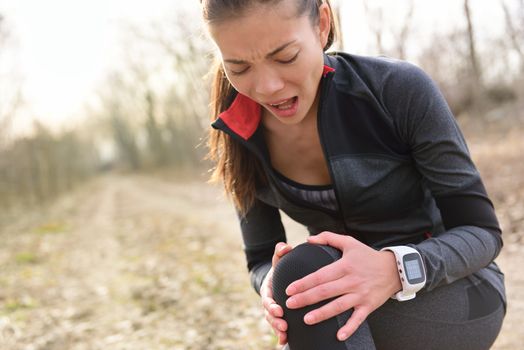 Sport and fitness injury - Female runner with hurting knee. Running woman screaming in pain during run wearing a smartwatch. Painful joint during workout.