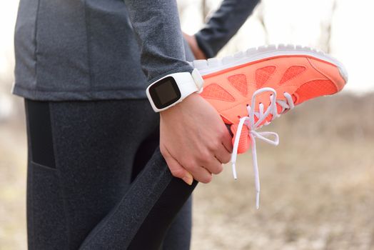 Running stretching - runner wearing smartwatch. Closeup of running shoes, woman stretching leg as warm-up before run with sport activity tracker watch at wrist to monitor the heart rate during cardio.