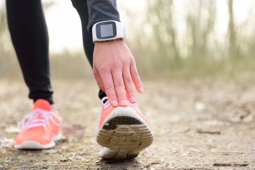 Runner stretching leg before run. Closeup of running shoes of a female jogger touching toe wearing a wearable tech - sportswatch activity tracker or smartwatch used as a heart rate monitor for cardio.