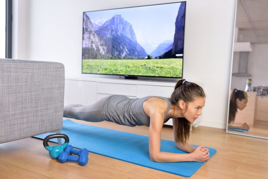 Living room fitness workout - girl doing plank exercises to exercise core at home. Young Asian woman training muscles in front of the TV as part of a healthy lifestyle without going to the gym.