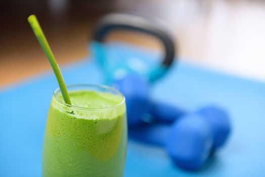 Green smoothie and dumbbells weights on yoga mat at the gym - fitness concept. Clean eating and detox with vegetable and spinach drink as part of the latest food trend in living healthy.