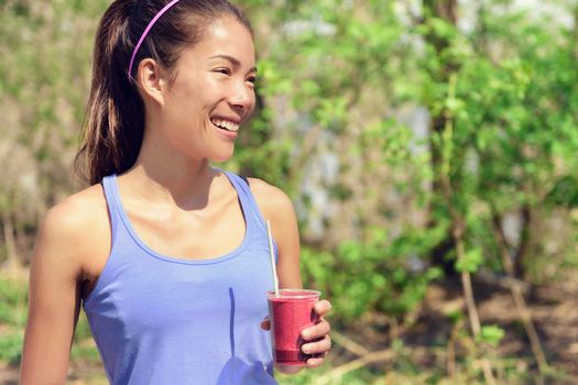 Healthy Asian woman drinking fruit smoothie drink in outdoor forest park during summer. Young fit girl holding plastic cup clean eating for detox cleansing with berry or beet juice as part of a diet.