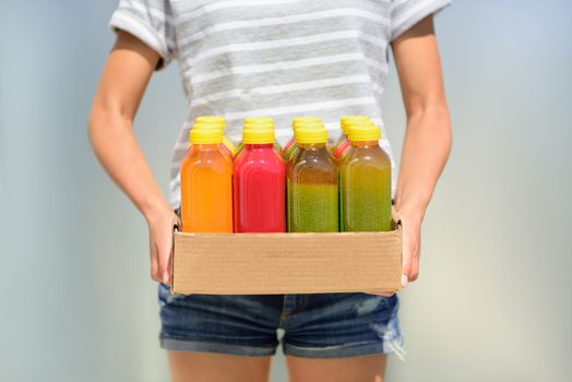 Woman holding delivery box of freshly cold pressed fruit and vegetable juice bottles. Closeup of female person carrying organic raw juices. Juicing is a food trend for diet cleanse detox.