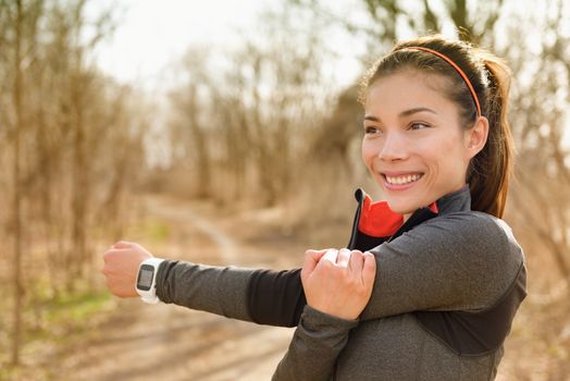 Fitness woman stretching arms with smartwatch before running or cardio workout. Happy Asian girl doing warm-up before jogging with heart rate monitor in outdoor park during autumn.