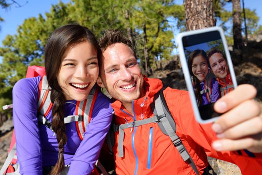 Happy friends hikers taking selfie on hiking trip. Couple posing for self-portrait picture on smartphone during summer holidays vacation travel camping and backpacking. Young multiracial couple.