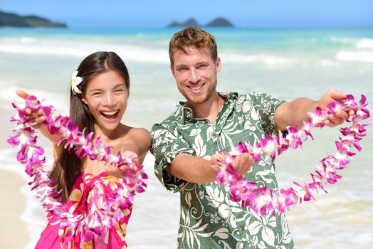 Welcome to Hawaii - Hawaiian people showing giving leis flower necklaces as welcoming gesture for tourism. Travel holidays concept. Asian woman and Caucasian man on white sand beach in Aloha clothing.