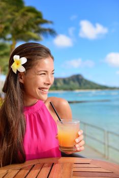 Cocktail woman drinking alcohol drinks at beach bar resort in Waikiki, Honolulu city, Oahu, Hawaii, USA. Asian girl tourist looking at camera toasting a glass of strawberry Hawaiian drink at sunset.