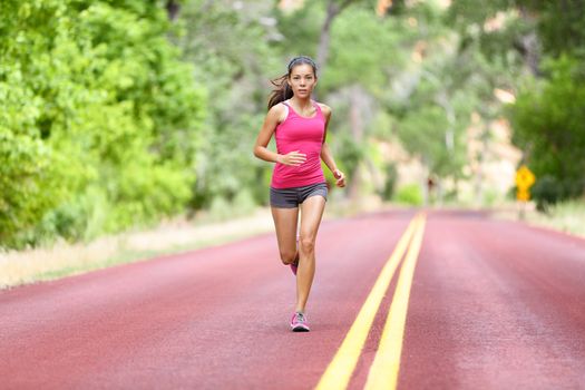 Running fit woman - female runner training outdoors jogging on red road in amazing landscape nature. Fit beautiful fitness model working out outside in summer.