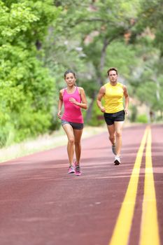 Running Health and fitness. Runners on run training during fitness workout outside on road. People jogging together living healthy active lifestyle outside in summer. Full body length of woman and man