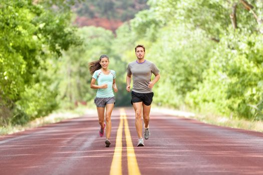 Running Health and fitness. Runners on run training during fitness workout outside on road. People jogging together living healthy active lifestyle outside in summer. Full body length of woman and man