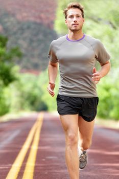 Man running on road. Sport and fitness runner training for marathon run doing workout outdoors in summer. Male athlete sports model fit and healthy aspirations.
